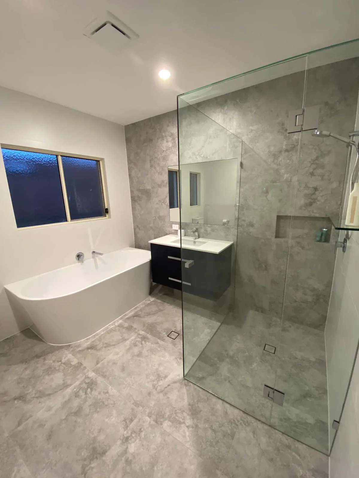 Bathroom with stone-look tiles, freestanding bath and frameless shower